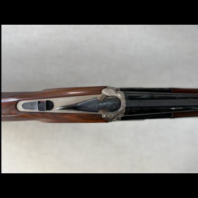 Espingarda com armação prateada gravada e madeira castanha vista de cima.