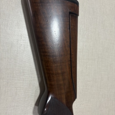 Coronha de arma de fogo em madeira escura com acabamento polido encostada numa parede clara.