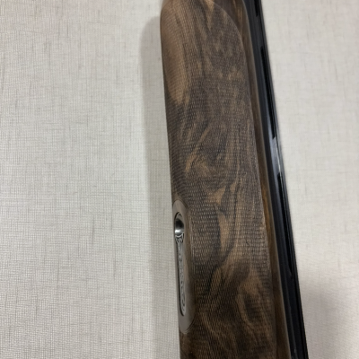 Guarda-mão de madeira castanho escuro com padrão e detalhe metálico numa espingarda