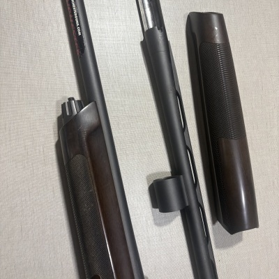 Peças de espingarda desmantelada em metal preto e madeira escura com texto WINCHESTERGUNS.COM