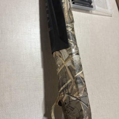 Espingarda camuflada em verde, bege e castanho com gatilho prateado e detalhes pretos