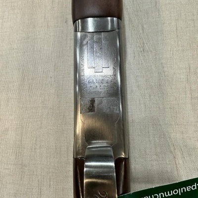 Espingarda de metal prateado e madeira castanha com gravações, sobre tecido bege