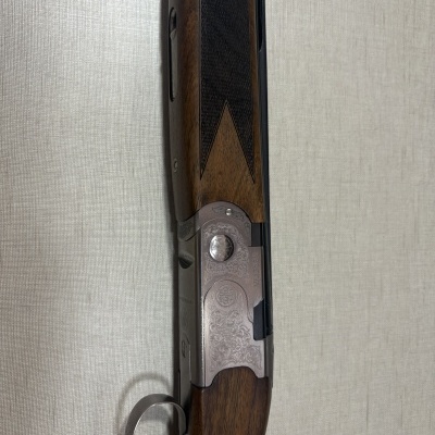 Espingarda com coronha em madeira castanha, parte metálica gravada com texto BERETTA e gatilho dourado