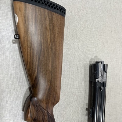 Peça traseira de arma com coronha em madeira e parte metálica preta em fundo claro