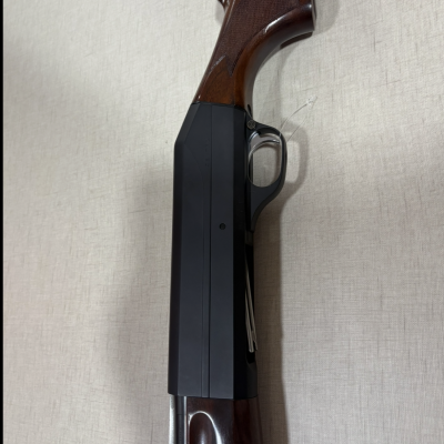 Espingarda com madeira castanha e metal preto sobre fundo cinzento claro.