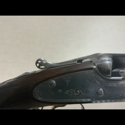 Detalhe lateral de uma arma de caça com metal gravado e madeira escura