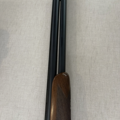 Espingarda de canos duplos com coronha em madeira e acabamento metálico preto.