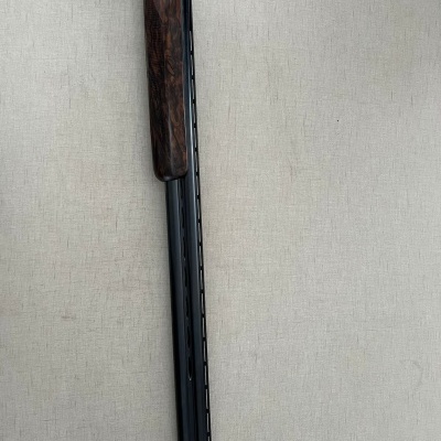 Espingarda dupla com madeira escura e cano preto, sobre fundo bege.