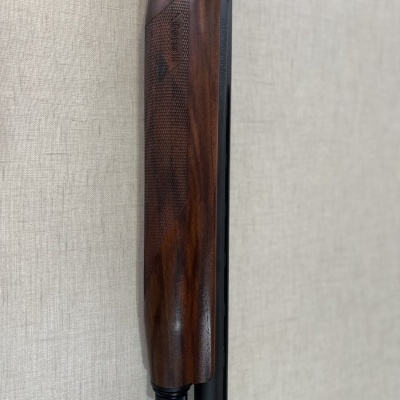 Empunhadura de madeira castanha escura e cano metálico preto de arma de fogo em fundo bege.