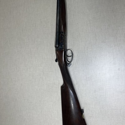 Espingarda de canos duplos e madeira escura encostada numa parede clara