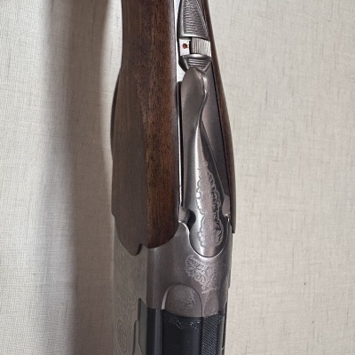 Espingarda com madeira castanha e metal prateado gravado em fundo branco.