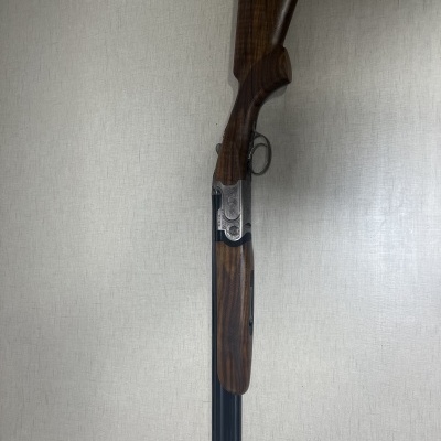 Espingarda de canos duplos com madeira castanha e metal preto encostada numa parede clara