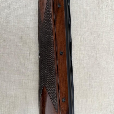 Parte da espingarda com madeira castanha, parafusos pretos e metal prateado com gravuras