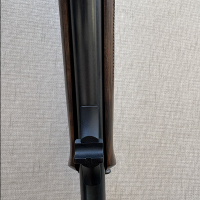 Parte superior de uma arma de fogo com madeira escura e metal preto fosco