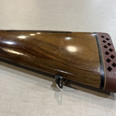 Coronha de espingarda em madeira polida com proteção de borracha vermelha próxima ao final