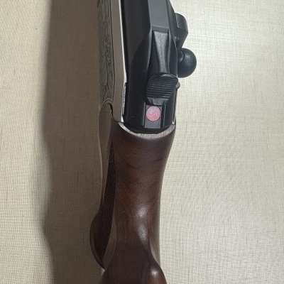 Espingarda com cabo de madeira e corpo metálico preto em fundo bege