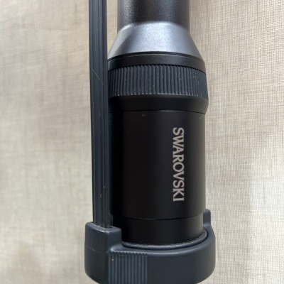 Parte de objeto óptico preto com marca SWAROVSKI em fundo de tecido bege