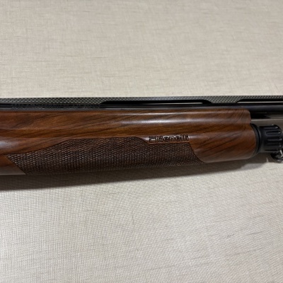 Espingarda Benelli com madeira e metal negro sobre superfície clara.