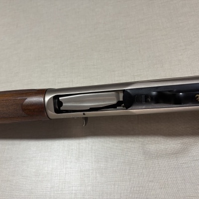 Espingarda com coronha em madeira castanha e acabamento em metal prateado e preto sobre superfície clara