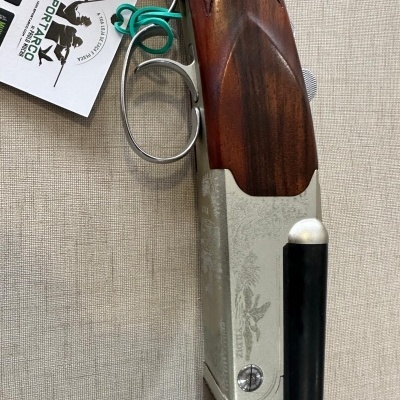 Espingarda com cabo de madeira castanha e metal prateado gravado, etiqueta SPORTARGO pendurada.