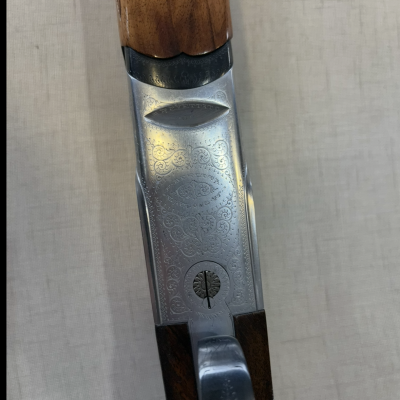 Parte central de arma de fogo com cabo em madeira clara e detalhes metálicos gravados em prateado