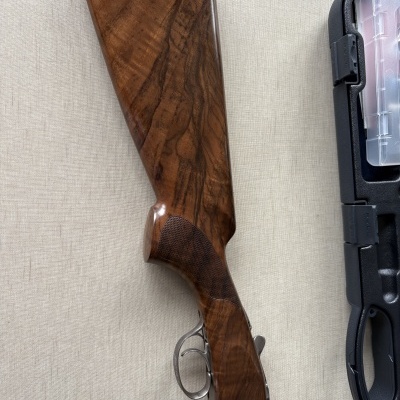 Espingarda com coronha em madeira polida castanho escuro e caixa preta ao lado.