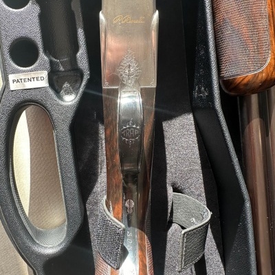 Espingarda com acabamento metálico e cabo de madeira em caixa preta com etiqueta PATENTED