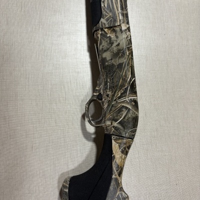 Arma de caça camuflada com padrão Realtree MAX-7, foco na parte traseira e gatilho.