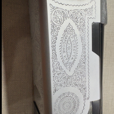 Arma com gravações decorativas e texto BERETTA GARDONE VT em fundo têxtil