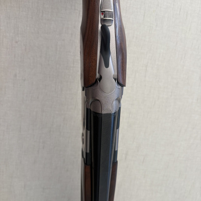 Espingarda com coronha de madeira e metal prateado sobre fundo branco.