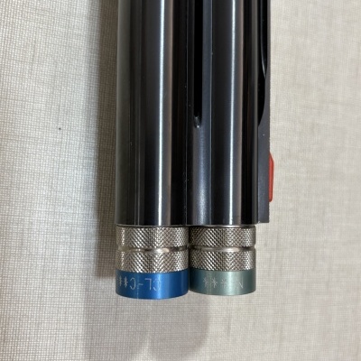 Extremidade metálica preta com anéis azuis e verdes com texto em fundo bege.