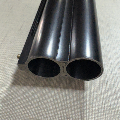 Cano duplo de espingarda em metal preto sobre superfície bege.