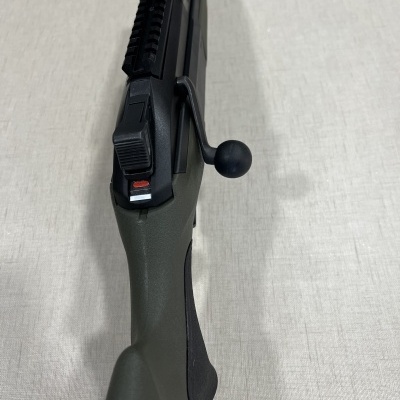 Espingarda de caça com cabo sintético cinzento e ferrolho preto sobre superfície clara