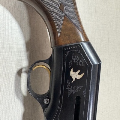 Parte de arma de fogo com cabo madeira castanha e corpo metálico preto com gravura dourada