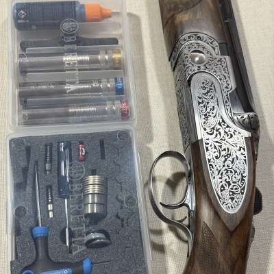 Espingarda Beretta com detalhes gravados, cantonada em madeira, caixa de ferramentas transparente com acessórios