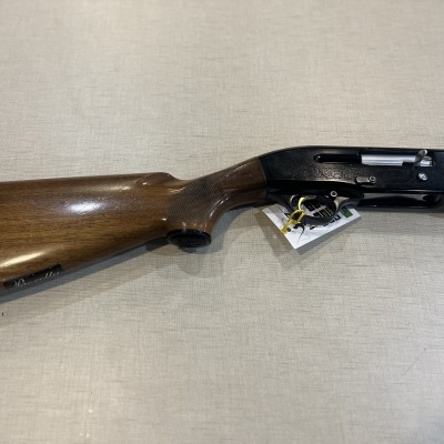 Espingarda com coronha em madeira e corpo metálico preto sobre superfície bege