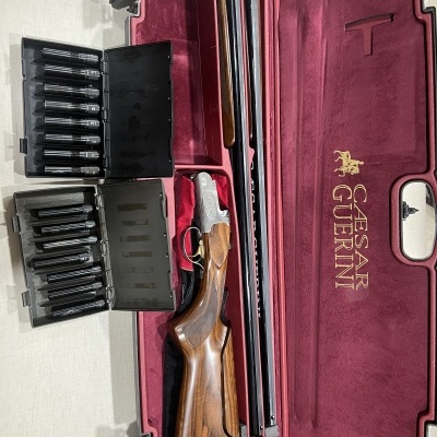 Case vermelho de veludo com espingarda de madeira e caixas pretas com carregadores