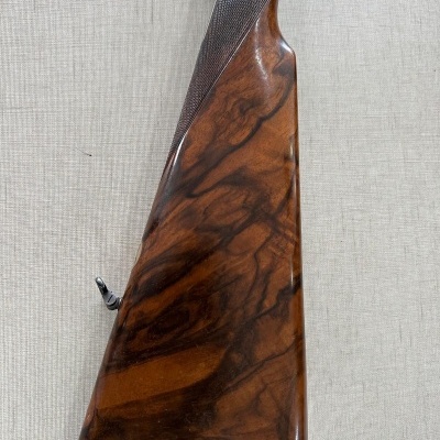 Coronha de espingarda em madeira polida com padrão escuro sobre superfície bege