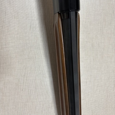 Espingarda com cano duplo preto e madeira castanha num fundo cinzento claro