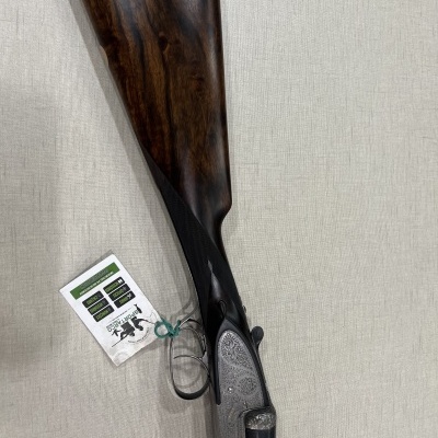 Espingarda com coronha em madeira escura e caixa de aço gravada em fundo bege
