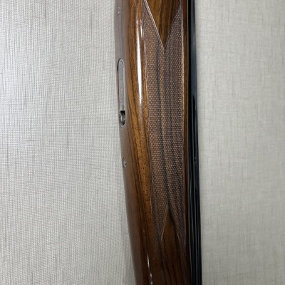 Espingarda com acabamento em madeira polida castanha e detalhes entalhados apoiada contra superfície cinzenta