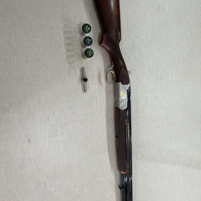 Espingarda de canos lado a lado com acessórios ao lado sobre superfície clara