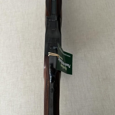 Espingarda de madeira e metal com etiqueta verde sobre tecido cinzento