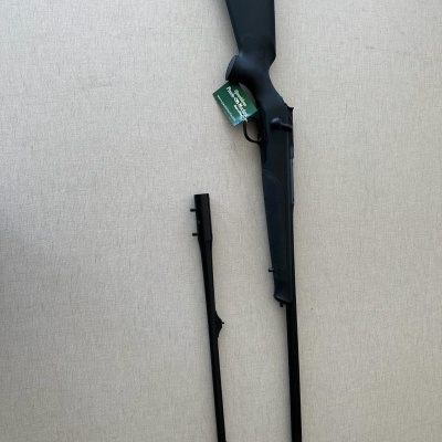 Rifle preto com dois canos, um ligado e outro separado, sobre superfície cinzenta