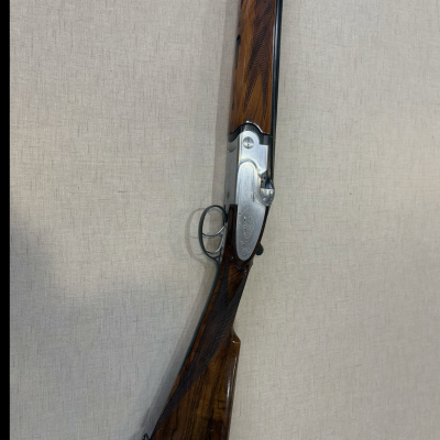 Espingarda com madeira castanha e parte metálica prateada pendurada num fundo bege