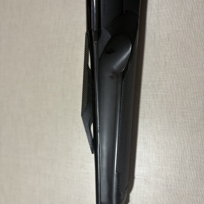 Espingarda preta com punho antiderrapante encostada numa parede bege clara.