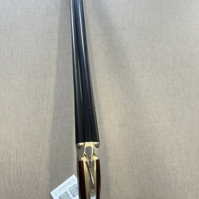 Espingarda de canos duplos com cabo em madeira escura e acabamento metálico, sobre superfície bege com papel ao lado.