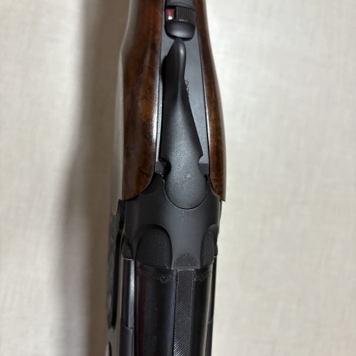 Arma com coronha de madeira castanha e corpo metálico preto fosco vista de cima