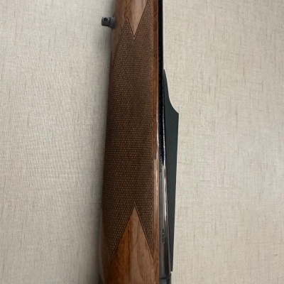 Parte lateral de arma com cabo de madeira castanha texturizada junto a parede bege