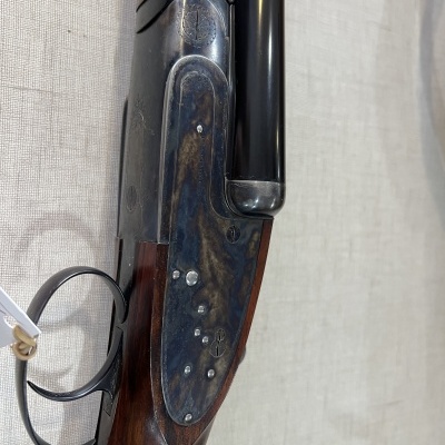 Escopeta com madeira escura e acabamento metálico azul em fundo bege